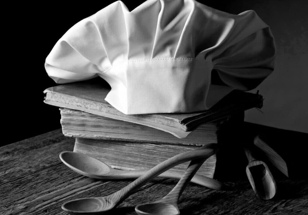Old culinary books , chef hat and wooden spoons . Kitchen accessories on the old wooden table .